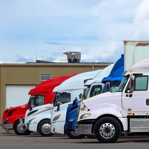 Fleet of colorful semi-trucks parked in a row outside a warehouse