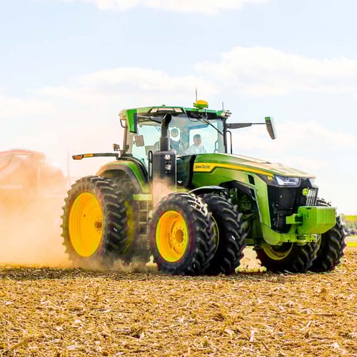 John Deere tractor working in a harvested field, kicking up dust during agricultural operations