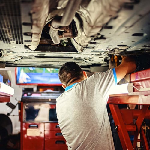 Auto mechanic working underneath a raised vehicle in a repair shop