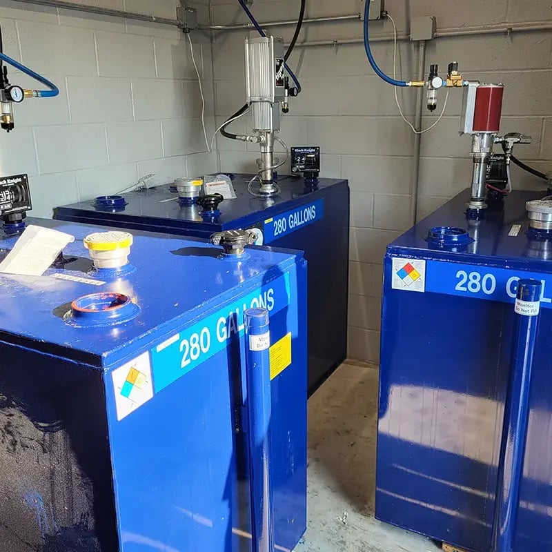 Three blue 280-gallon chemical storage tanks with fluid dispensing systems in an industrial facility