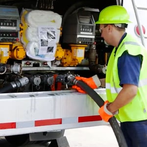 Worker in safety gear refueling a truck using a large hose at an industrial fueling station
